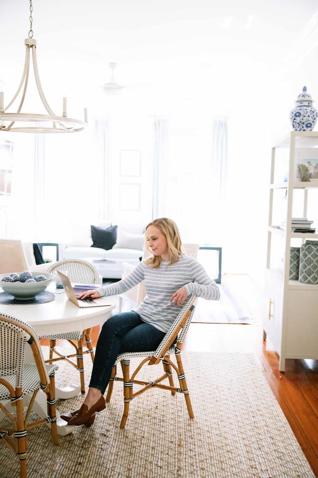 Digital Grace Design owner, Sarah, sits at white round table working on laptop in blue and white striped sweater